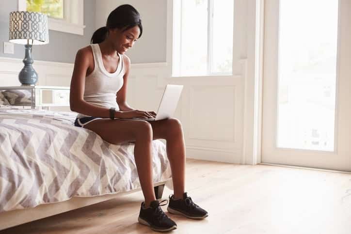 woman in athletic shoes sitting on bed with laptop