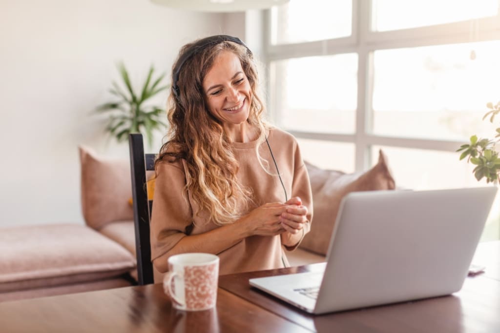 woman wearing a headset smiling and looking at a laptop computer