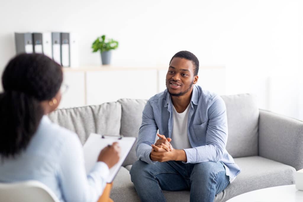 Man sitting on couch talking to a coach with a clipboard