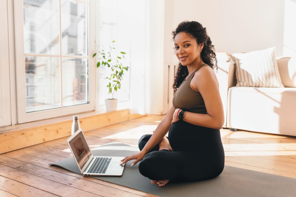 Pregnant woman sitting on yoga mat on her laptop